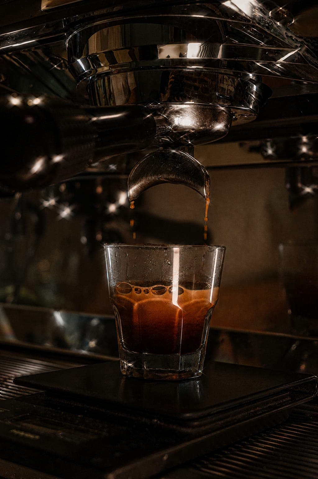 Espresso extrayéndose en un vaso, con la máquina desenfocada de fondo